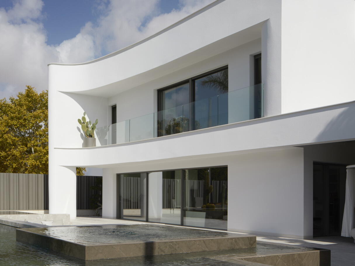 Integrated into the backyard’s sculptural layout is a swimming pool that becomes part of the residence’s calm and curated outdoor flow. A raised spa area flows seamlessly into the main pool, while long the left edge, lush tropical foliage adds a burst of green and softens the contrast with the crisp lines of the modern gray fence.