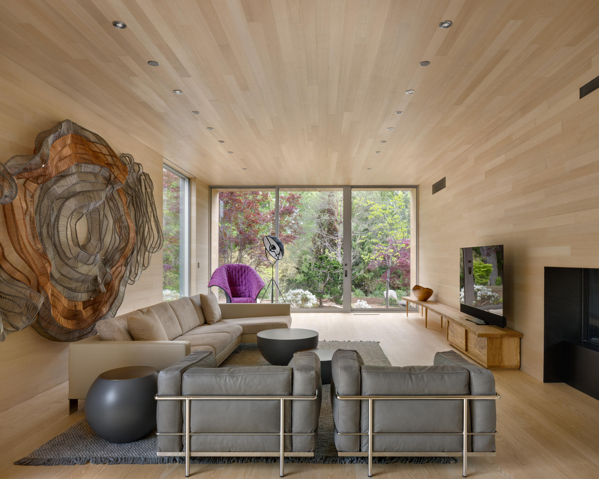In this wood-lined living room, floor-to-ceiling glass walls bring uninterrupted views of a cultivated landscape into serene interior volumes.
